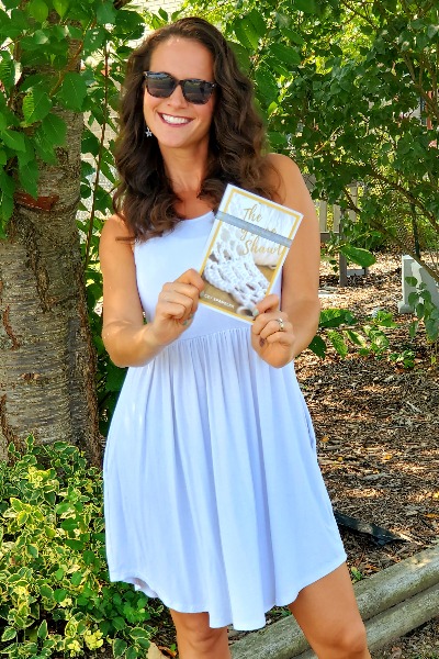 woman smiling beside a tree holding a book