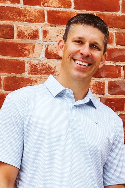 man smiling at camera in front of a red brick wall